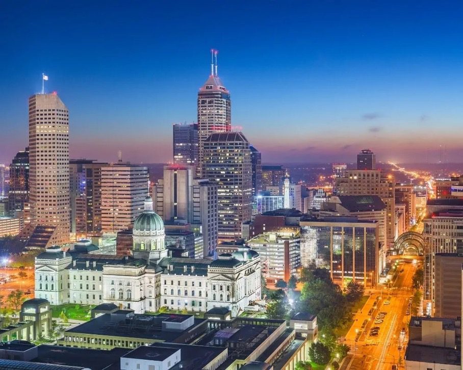 Indianapolis skyline at night, featuring the Indiana Statehouse surrounded by illuminated buildings and city streets